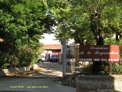Entree du Domaine de la Reynardiere : portail ouvert sur la cour, batiments du chai au fond, vehicules, arbres et lauriers-roses, grand panneau rouge 'Domaine de la Reynardiere - Degustation Vente'. Vue d'ensemble du domaine identifiable. Porte une date/credit en surimpression (06 juin 2010, J-L Dio