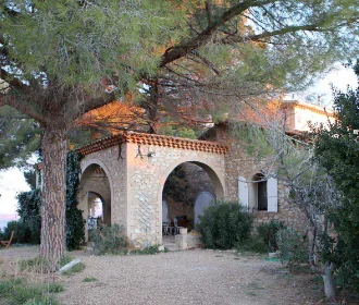 Le mas / batiment du domaine en pierre avec arcades et tuiles, niche sous un grand pin, cour en gravier. Architecture languedocienne traditionnelle du domaine. 330x280 (basse def).
