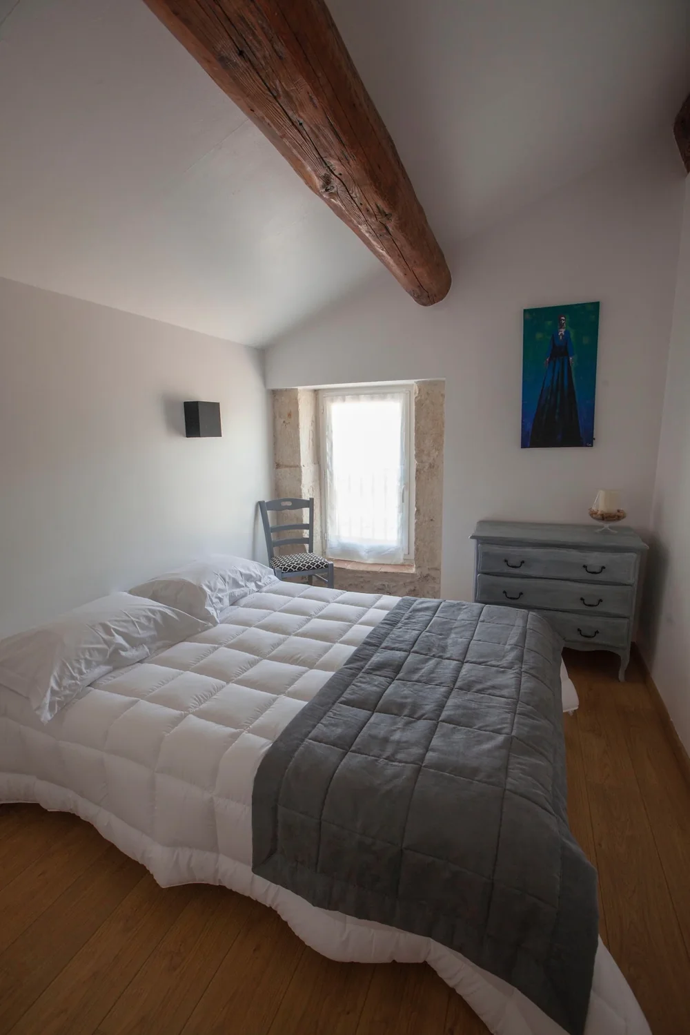 Chambre du gîte : lit double, poutre apparente, fenêtre en pierre, commode patinée. Intérieur d'hébergement soigné.