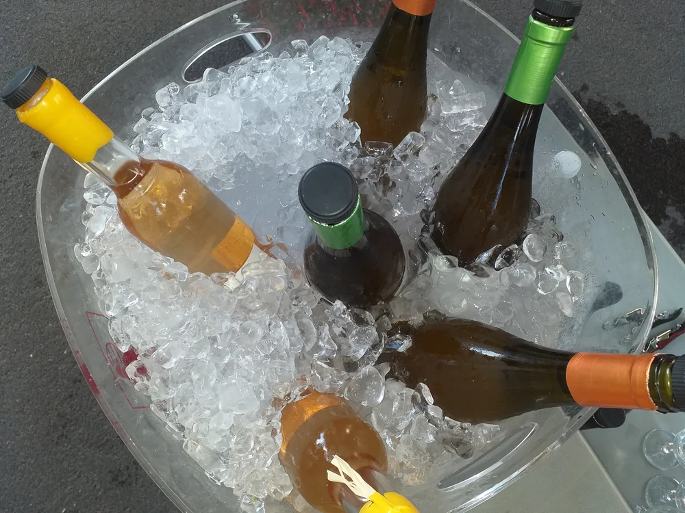 Bouteilles de vin (blancs/roses) rafraichissant dans une vasque transparente remplie de glacons, plan plongeant. Jolie photo lifestyle de mise en situation des bouteilles.