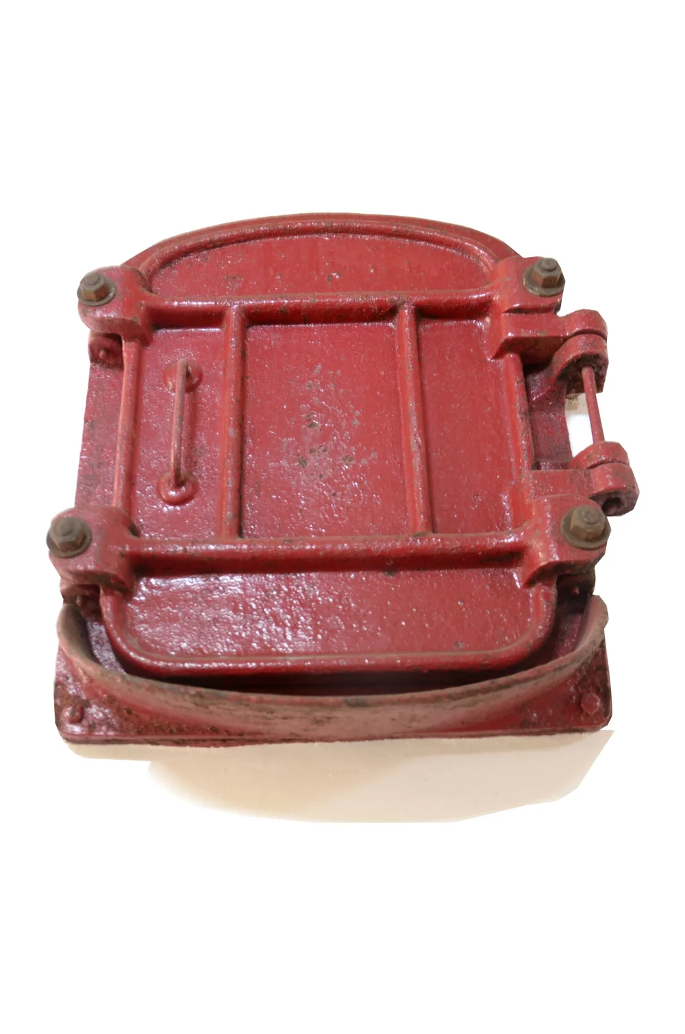 Porte/trappe en fonte rouge d'une ancienne cuve a vin en beton, posee sur fond blanc. Objet patrimonial du chai. Authentique mais decontextualise (packshot d'objet). Modeste mais appartient bien a la cave.