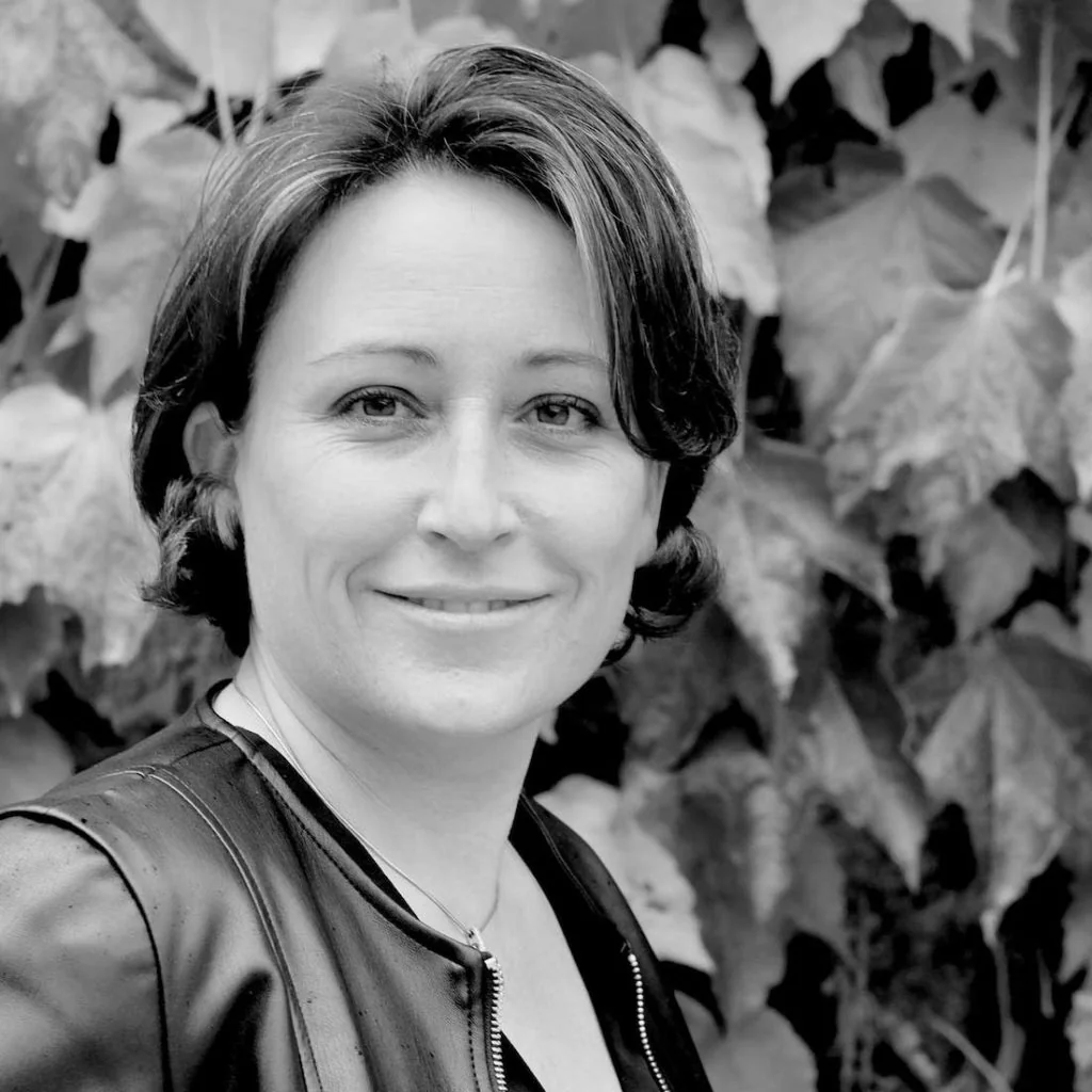Portrait noir et blanc d'Audrey, membre de l'equipe, souriante devant un mur de vigne vierge. Belle serie portraits equipe (1100x1100).